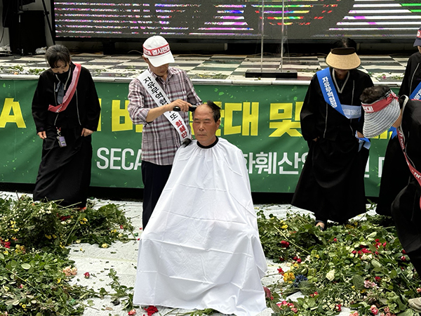 상복을 입은 여성 농민들이 꽃을 바닥에 던지는 퍼포먼스를 진행한 후 정윤재 김해대동화훼작목회장이 삭발식을 진행하고 있는 모습.